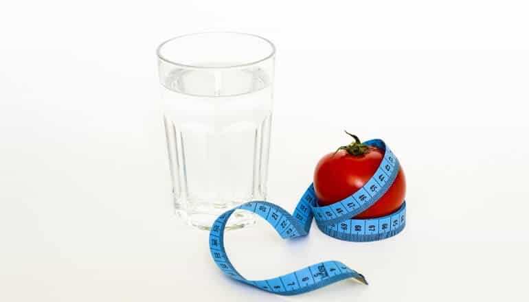 apple and glass of water with a waist tape measure on a table