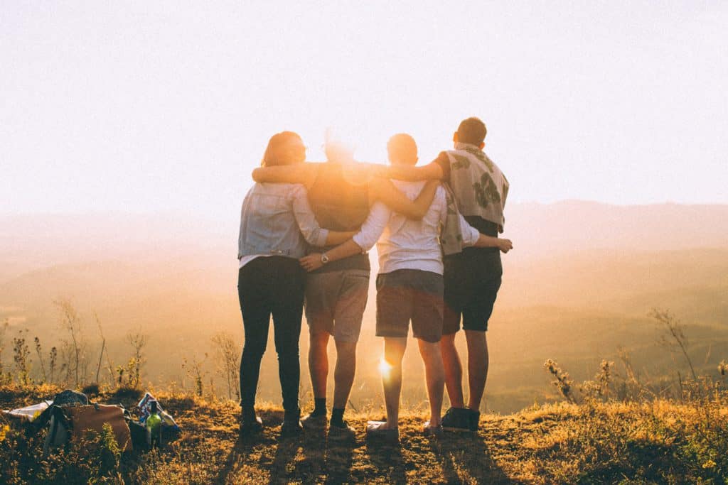 4 people standing on a hill in front of a sunset