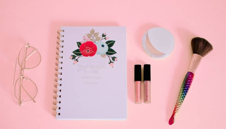 makeup glasses and a notebook on a pink table