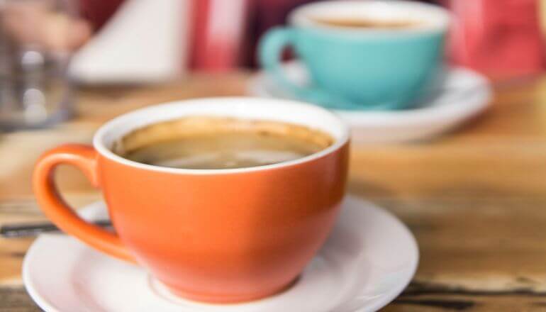 2 cups of coffee on white saucers, one cup is a cream orange the other is a light blue