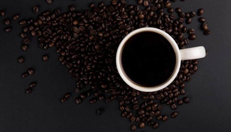 cup of coffee on table with beans around it