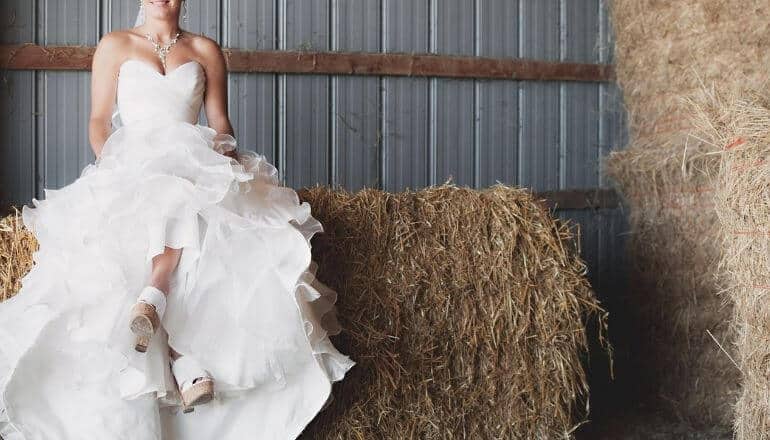 woman in wedding dress sitiing on haybale