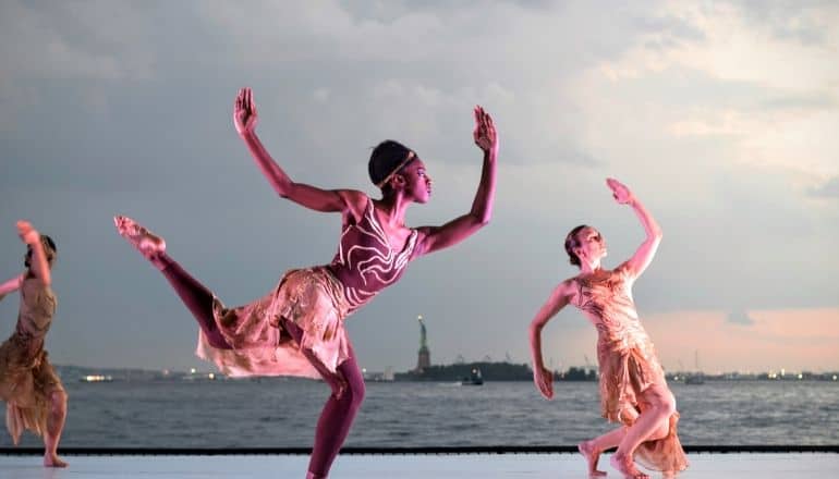 women dancing overlooking statue of liberty