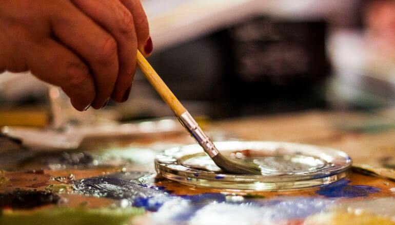 woman dipping paint brush into paint