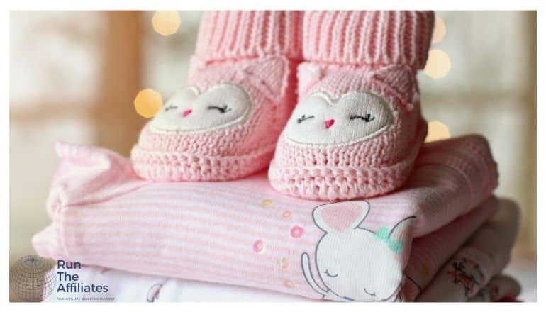 baby clothes in a folded stack with pink knitted boots on top