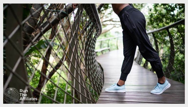 woman in activewear pants leaning on a metal fence on a walway in the forest