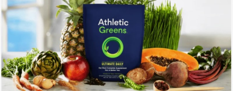athletic greens product with fruit and vegetables displayed behind it