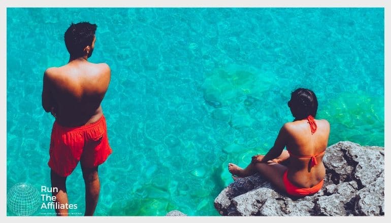 man and woman sitting on rocks next to the sea wearing red bathing suits