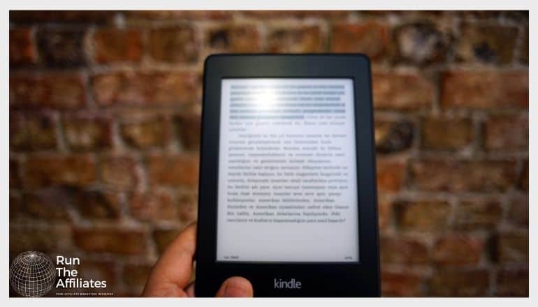 black kindle held in front of a brick wall with an ebook on screen