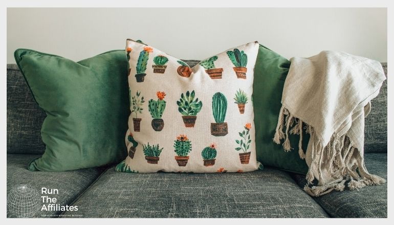 2 green throw pillows and a cactus themed pillow on a grey sofa with a white blanket draped over the back of the sofa