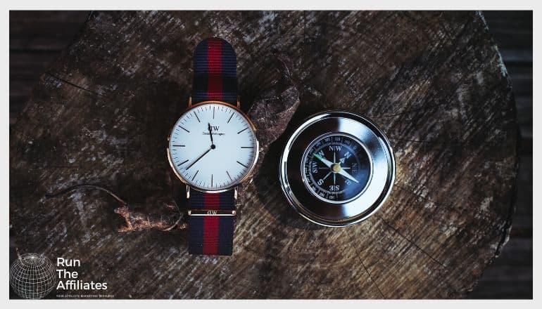 watch with red and black band sitting on a piece of wood next to a compass