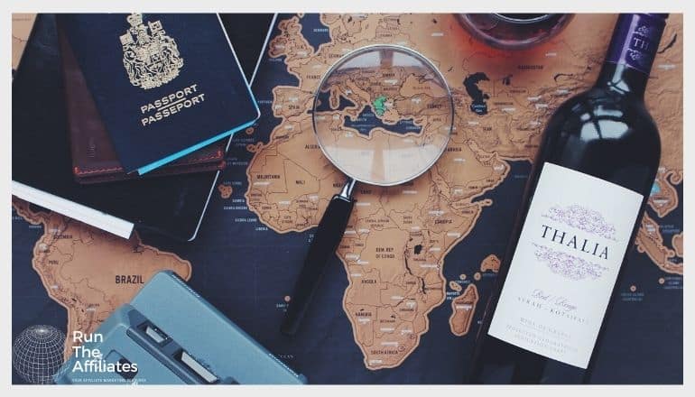 map on a table with a magnifying glass, passport, camera and a bottle of wine on top of it