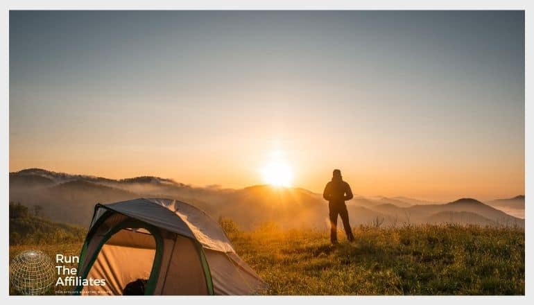 man camping at dawn with a tent in the forground and the rising sun in the background