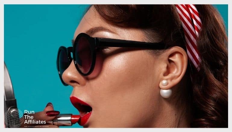 woman wearing sunglasses while applying red lipstick