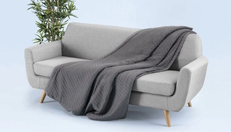grey honeybird weighted blanket resting on a light grey sofa with a green plat in the background