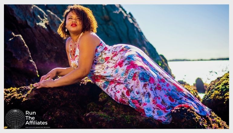 woman in a floral dress posing on a rock on the beach at sunset