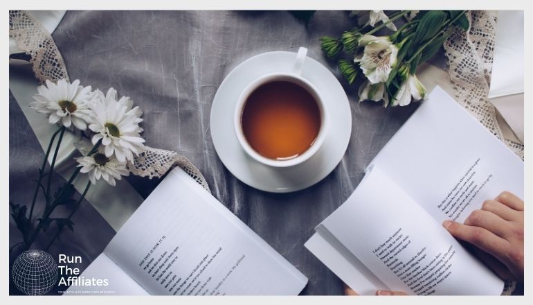 cup of tea on a table surrounded by open books and flowers